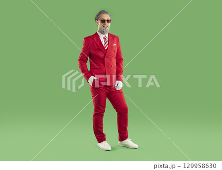 Portrait of funny man wearing red Christmas costume standing on green studio background 129958630