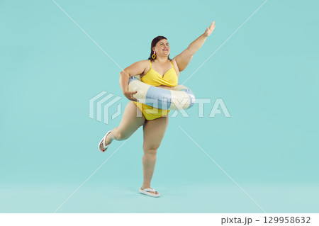 Funny young fat woman in yellow bikini and in rubber ring having fun isolated on blue background. 129958632