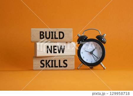 Build New skills symbol. Concept word Build New skills on wooden blocks with alarm clock. Beautiful orange background. Business and Build New skills concept. Copy space 129958718