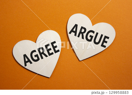 Agree or Argue symbol. Concept word Agree or Argue on wooden hearts. Beautiful orange background. Business and Agree or Argue concept. Copy space 129958883