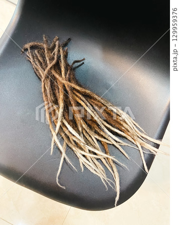 Cut dreadlocks with natural black color and light tips on chair. Concept of hair, style, identity and transformation. 129959376