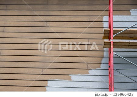 House exterior renovation project with scaffolding and partially painted walls in progress during daylight hours 129960428