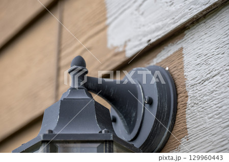 Wall-mounted outdoor light fixture being painted on a weathered wooden surface in daylight Wall-mounted outdoor light fixture being painted on a weathered wooden surface in daylight 129960443