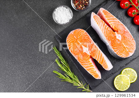 Fresh raw salmon or trout steaks with tomatoes, spices, rosemary and lime on black stone background Fresh raw salmon or trout steaks with tomatoes, spices, rosemary and lime on black stone background 129961534