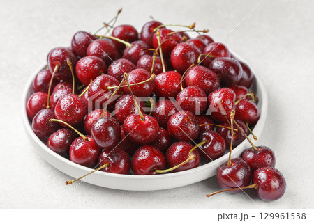 White plate full of fresh ripe red sweet cherry with water drops on white textured bakground 129961538