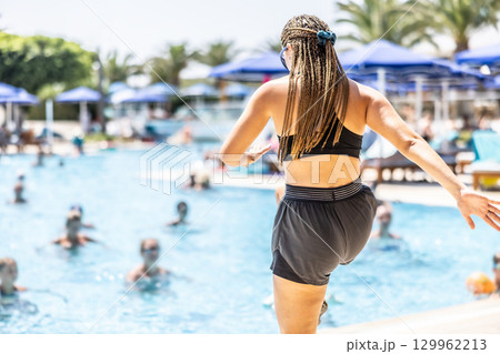 A young female Sports Animator is doing water aerobics for people in the pool of a hotel resort 129962213