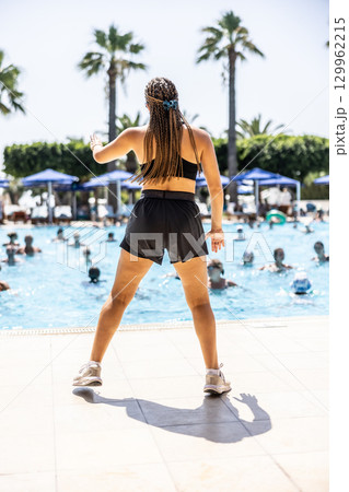 A young female Sports Animator is doing water aerobics for people in the pool of a hotel resort A young female Sports Animator is doing water aerobics for people in the pool of a hotel resort 129962215