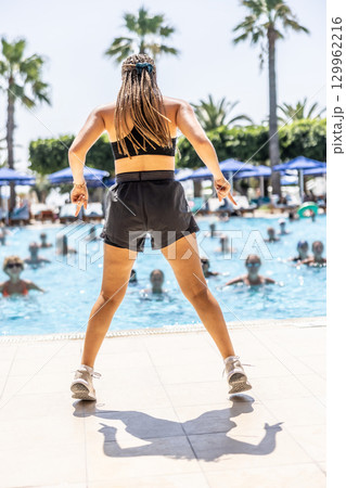 A young female Sports Animator is doing water aerobics for people in the pool of a hotel resort 129962216