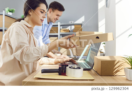 Woman working in logistics center with male colleague preparing order for client in warehouse 129962304
