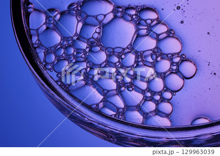 Serum with bubbles in a petri dish on a purple background. 129963039