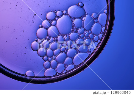 The texture of a cosmetic serum with a trail of bubbles on a purple background. 129963040