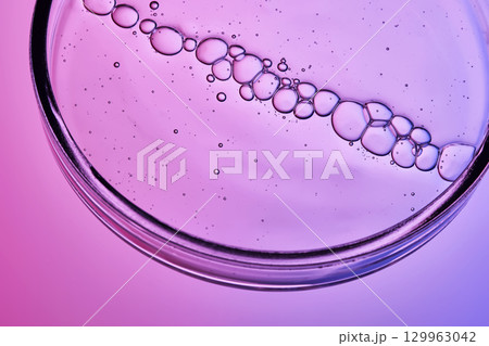Serum with bubbles in a petri dish on a purple background. 129963042