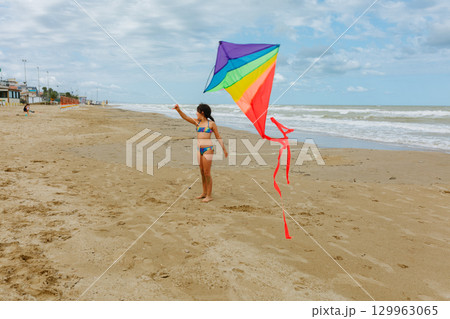 wide angle view of a girl flying a rainbow kite on the beach 129963065