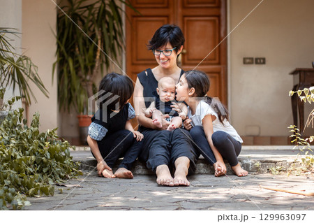 portrait of smiling mother sitting with three children in front of the house 129963097