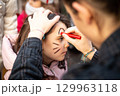 side view of a child face painting at carnival 129963118