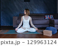 woman sitting in lotus yoga pose doing exercise at home looking aside 129963124
