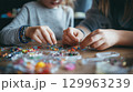 Children crafting colorful beaded jewelry together with focus and creativity 129963239