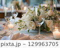 Elegant wedding table setting with white floral centerpiece, candles, and wine glasses creating a romantic atmosphere.  129963705
