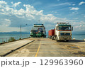 Cargo truck leaving a ferry at a seaside dock under a clear blue sky with scattered clouds. 129963960