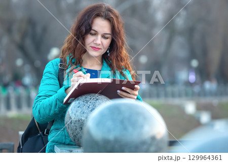 Woman in teal jacket sketches in a notebook near round stone sculptures during daytime Woman in teal jacket sketches in a notebook near round stone sculptures during daytime 129964361