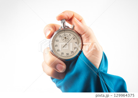 Hand holding a silver stopwatch in a bright setting during a timing event 129964375