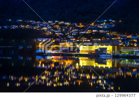Nighttime view of a Norwegian town reflecting on the water at dusk 129964377
