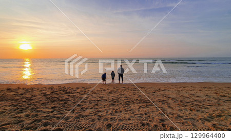 Father with two children stay on the sand beach near the sea. Sunset background. 129964400