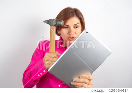 Woman expressing frustration while holding a hammer near a tablet in a studio setting Woman expressing frustration while holding a hammer near a tablet in a studio setting 129964414