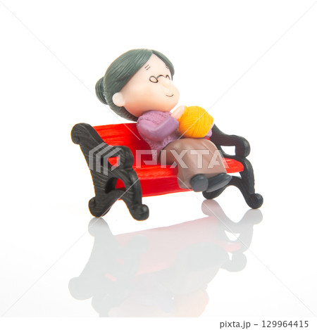 Miniature woman knitting on a red bench during a quiet afternoon 129964415