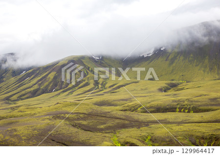 Explore the rugged beauty of Iceland's landscape with lush green hills and misty mountains 129964417