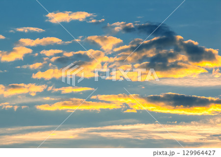 Vibrant sunset clouds illuminated by golden light in the evening sky above the horizon 129964427