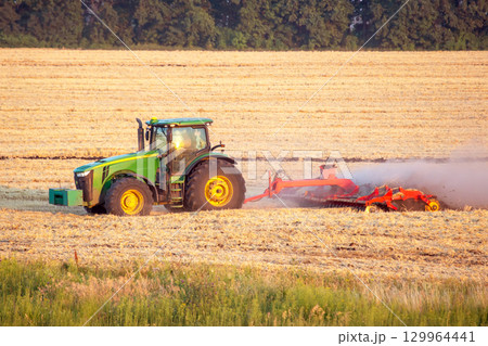 Tractor working on agricultural field during sunrise in golden light 129964441
