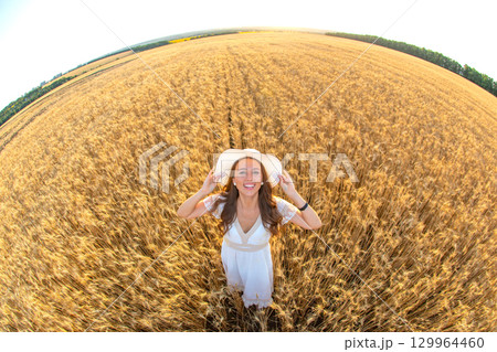 Woman in white dress enjoying summer in golden wheat field under sunny blue sky Woman in white dress enjoying summer in golden wheat field under sunny blue sky 129964460