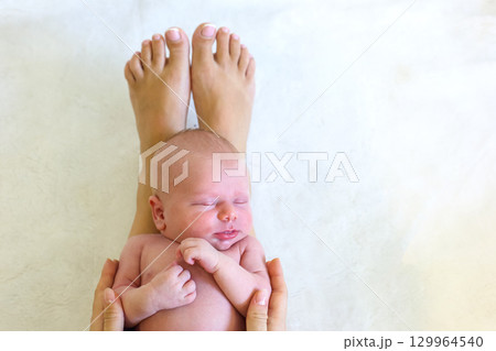 Newborn baby peacefully resting in hands with adult feet in view 129964540