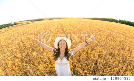 Woman enjoys sunny day in expansive golden wheat field with arms outstretched 129964553