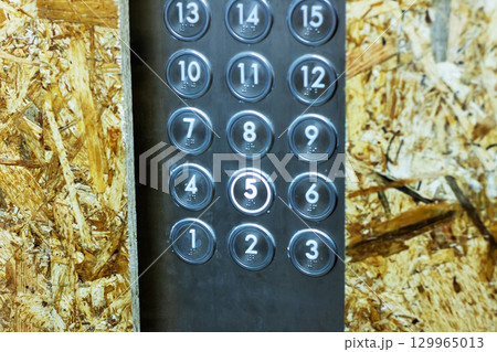 This is a closeup view of a modern elevator keypad set against a wooden panel 129965013