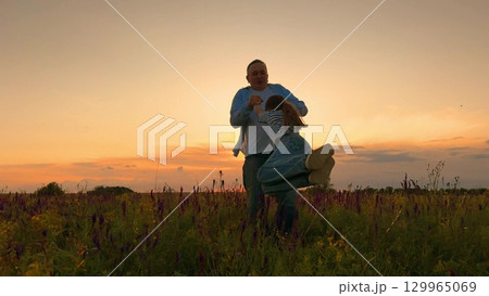Dancing in the sunset field, Father and daughter joy, Wildflower happiness, Evening warmth and laughter, Silhouette stories of love, Fields of joy and connection, Beautiful moments at dusk, Parental 129965069
