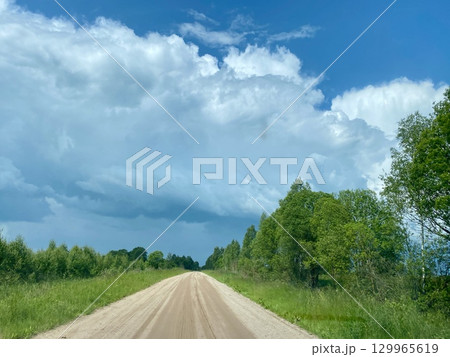 A Scenic Dusty Road Winding Its Way Through a Lush Green Landscape Beneath Dramatic Clouds 129965619