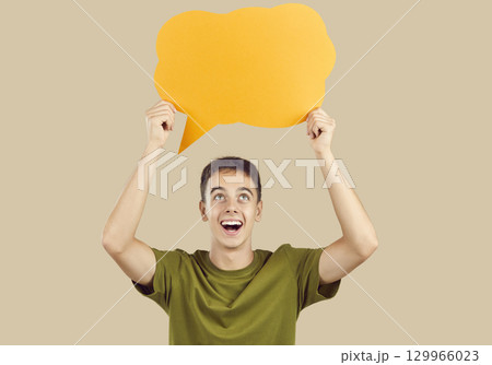 Happy young man holding orange speech balloon or thinking bubble on beige background 129966023