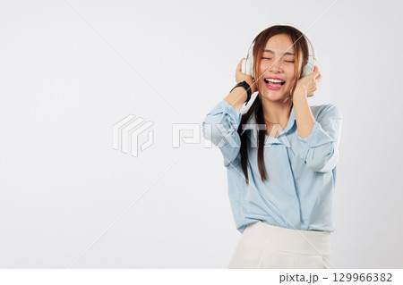 Music brightens her day as happy young Asian woman touches headphones and listening, while background music adds to the peaceful mood. isolated studio white background Music brightens her day as happy young Asian woman touches headphones and listening, while background music adds to the peaceful mood. isolated studio white background 129966382