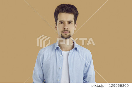 Portrait of smiling young man with neatly shaved beard and mustache, dressed in white T-shirt and blue shirt, confidently looking straight into the camera. 129966800