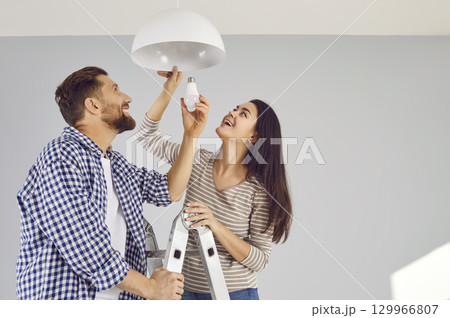 Happy husband and wife changing an energy-saving light bulb in the ceiling lamp together 129966807