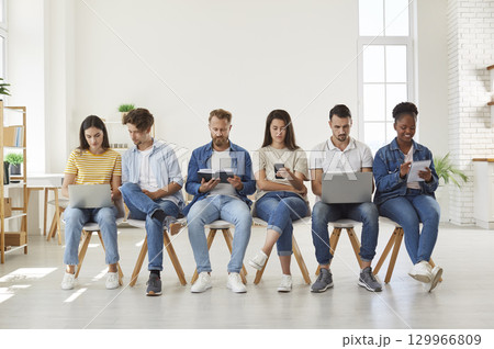 Multicultural young people using digital devices sitting in row Multicultural young people using digital devices sitting in row 129966809