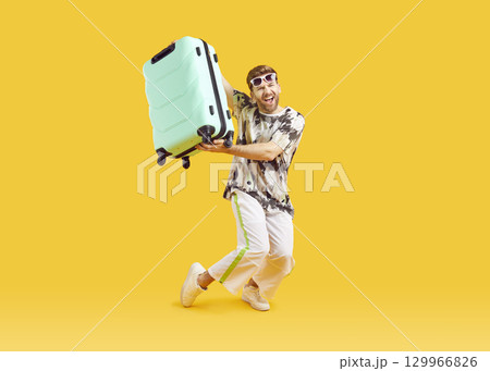 Funny young man in sunglasses with suitcase is going on summer holiday on yellow background. 129966826
