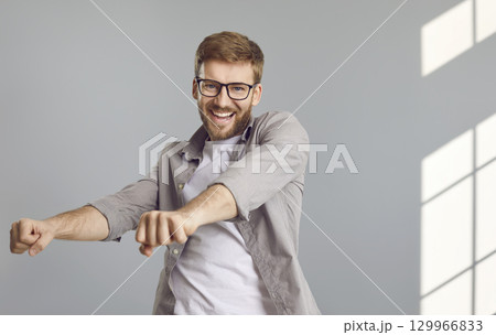 Happy, cheerful young man in a casual shirt and glasses is dancing and having fun 129966833