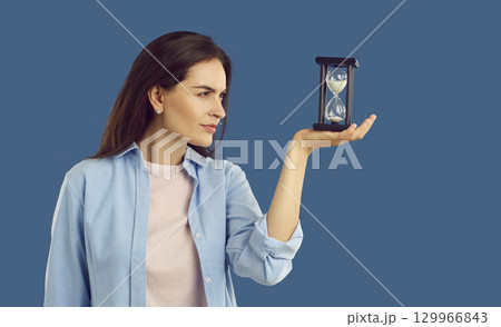 Young woman thinking while looking at sand glass that she is holding in her hand 129966843