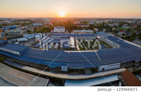 Aerial view of solar power plant with blue photovoltaic panels mounted on industrial building roof for producing green ecological electricity at sunset. Production of sustainable energy concept Aerial view of solar power plant with blue photovoltaic panels mounted on industrial building roof for producing green ecological electricity at sunset. Production of sustainable energy concept 129966871