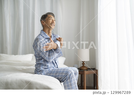 ベッドに座ってストレッチをするパジャマを着たシニア男性 ベッドに座ってストレッチをするパジャマを着たシニア男性 129967289