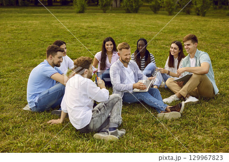 Diverse team of happy business students working together, sitting on grass in park and using laptop Diverse team of happy business students working together, sitting on grass in park and using laptop 129967823