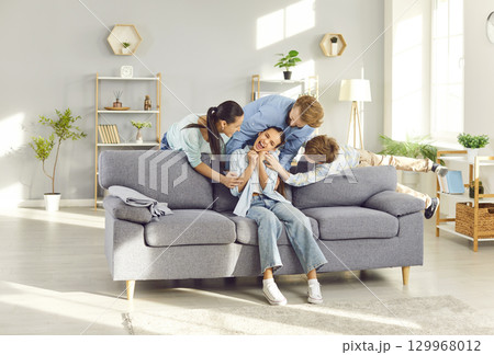 Happy laughing teenage child girl having fun tickling with parents and brother sitting at home Happy laughing teenage child girl having fun tickling with parents and brother sitting at home 129968012
